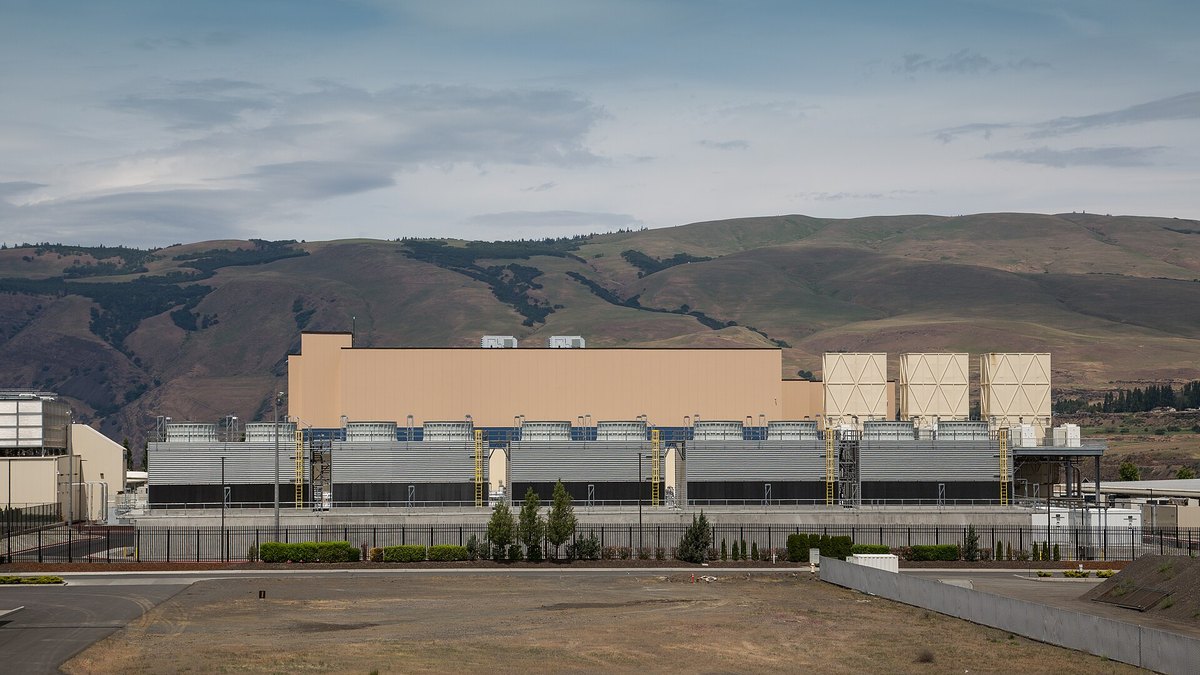 A data center building with a row of cooling units in front of it, below a ridge in The Dalles, Oregon