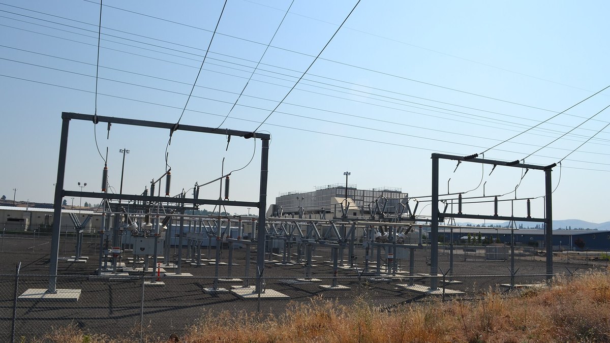 Overhead power lines and a switchyard in the foreground, with data center buildings behind them, The Dalles, Oregon