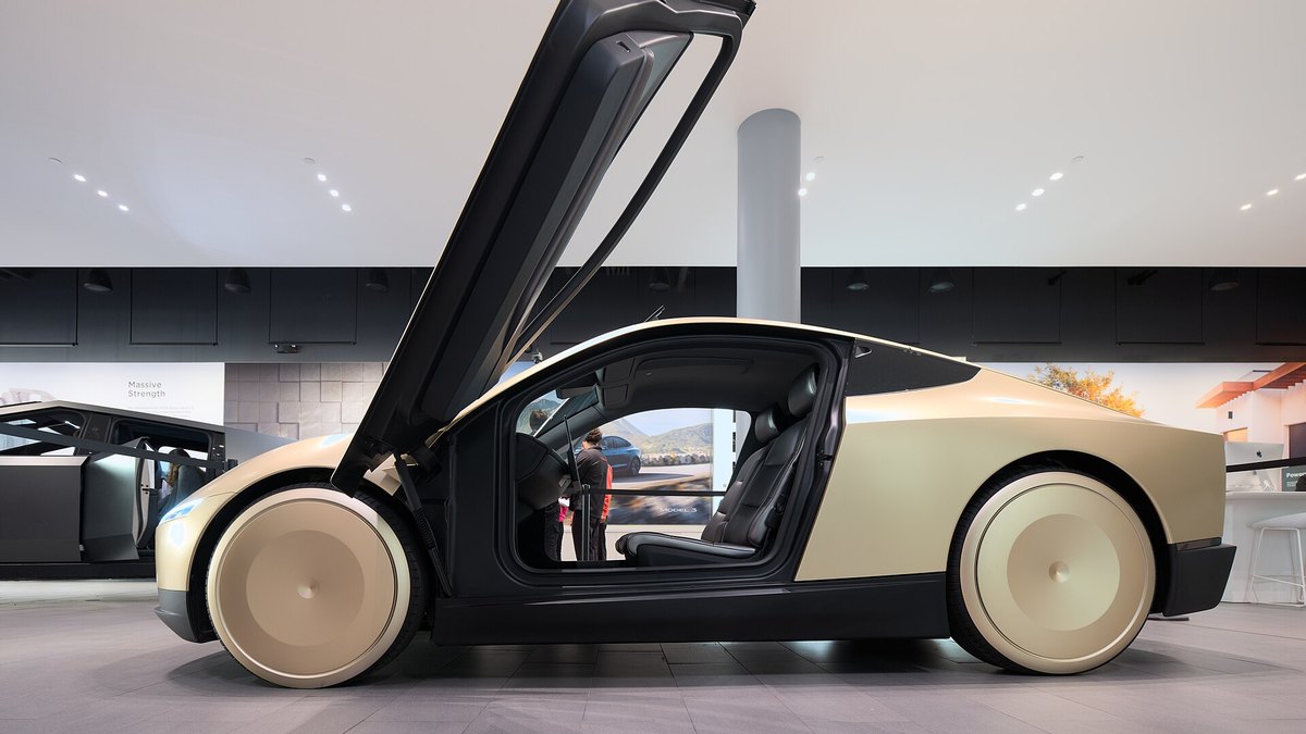 A gold Tesla Cybercab on display with its upward-opening door raised