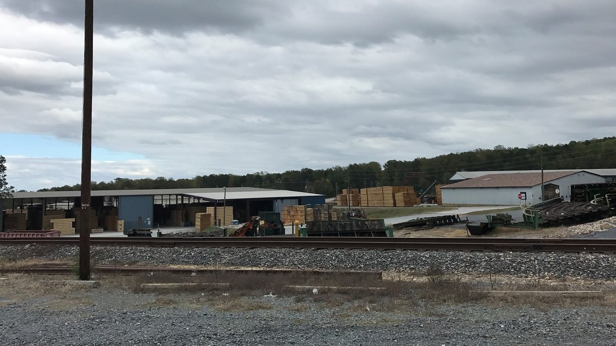 A lumber yard with covered storage sheds and stacked lumber packs beside a rail line in Troy, North Carolina