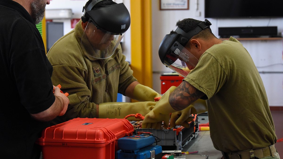 Airmen wearing insulated rubber gloves and face shields working on an exposed electric vehicle battery pack during a U.S. Air Force EV training course