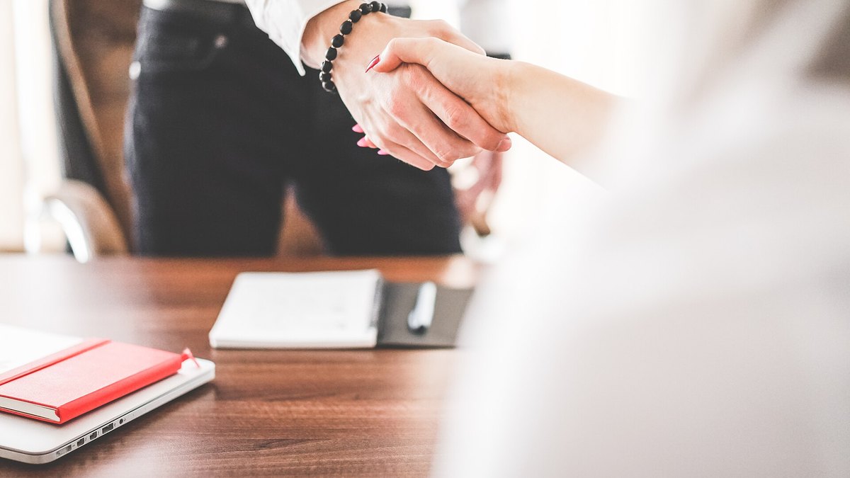 Two people shaking hands across an office desk