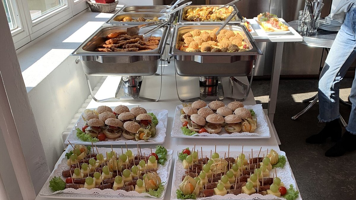 A catered buffet with chafing dishes, sliders, skewers and salads on a white table
