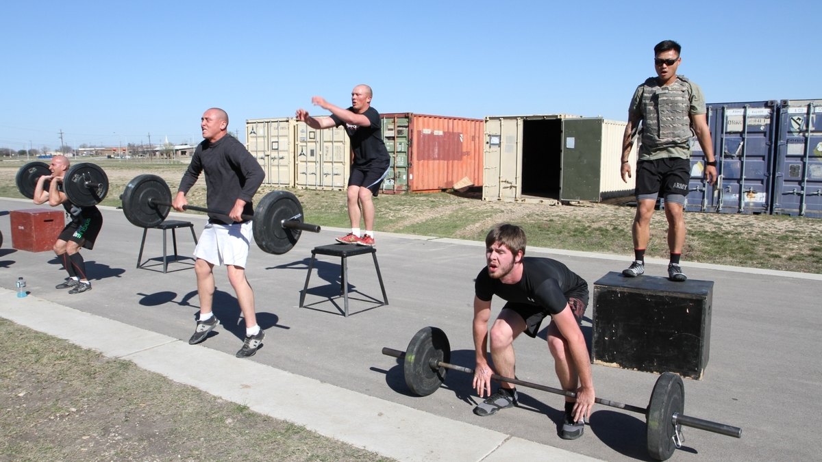 A group of athletes doing barbell and box-jump exercises in a coached workout