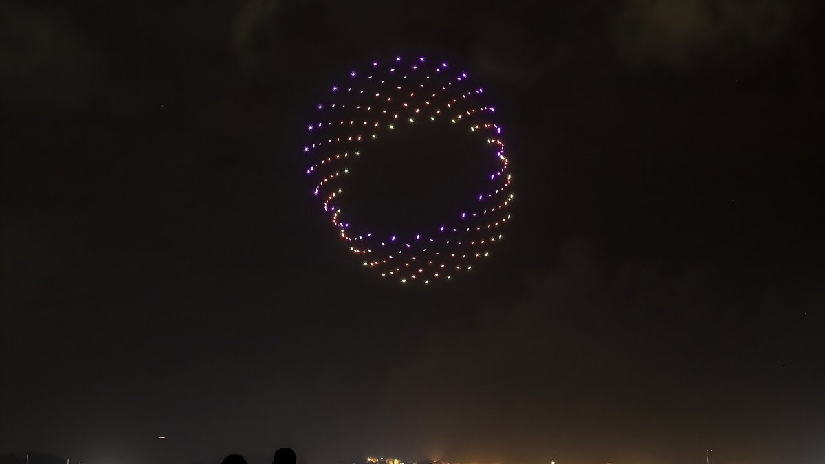 A drone light show forming a glowing spiral in the night sky over a harbor