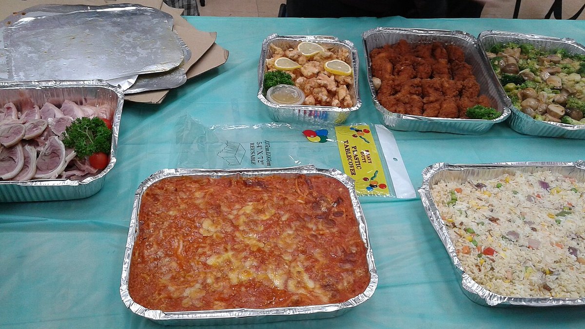 Foil catering trays of pasta, chicken and rice set out on a table
