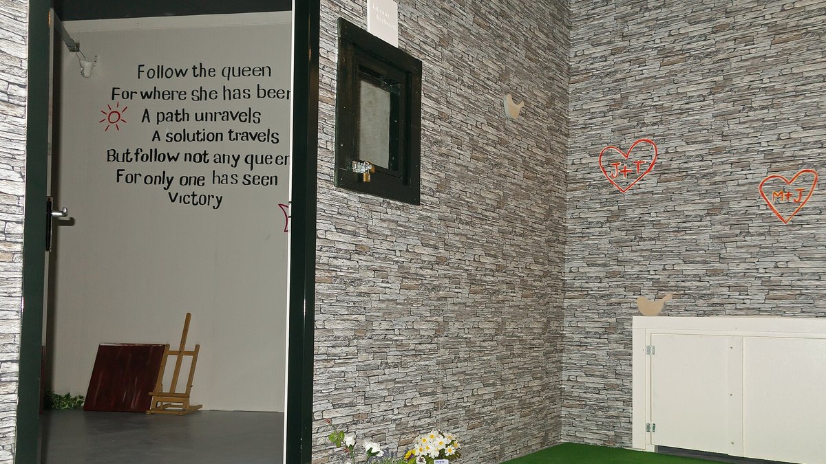 A bare-walled escape room set with a painted riddle on the wall and an open door