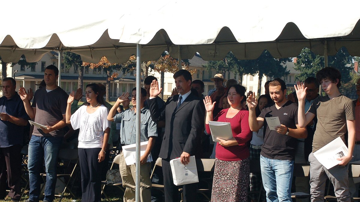 New citizens raising their right hands at an outdoor naturalization oath ceremony