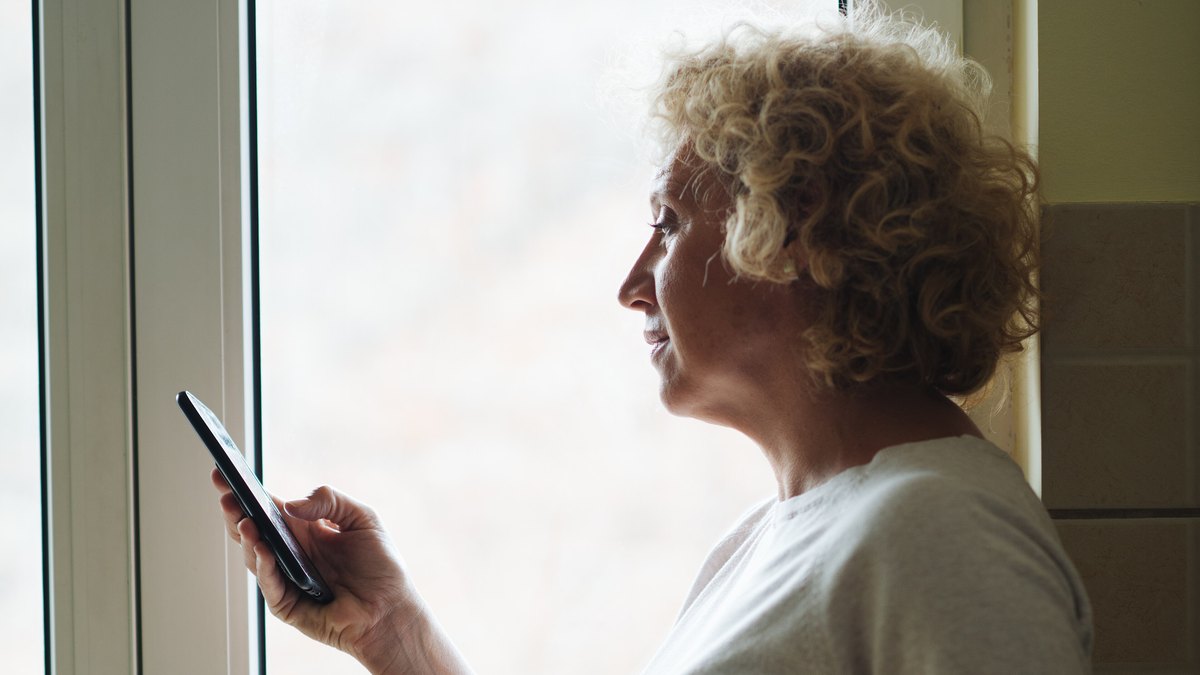 An older woman looking at her smartphone beside a window