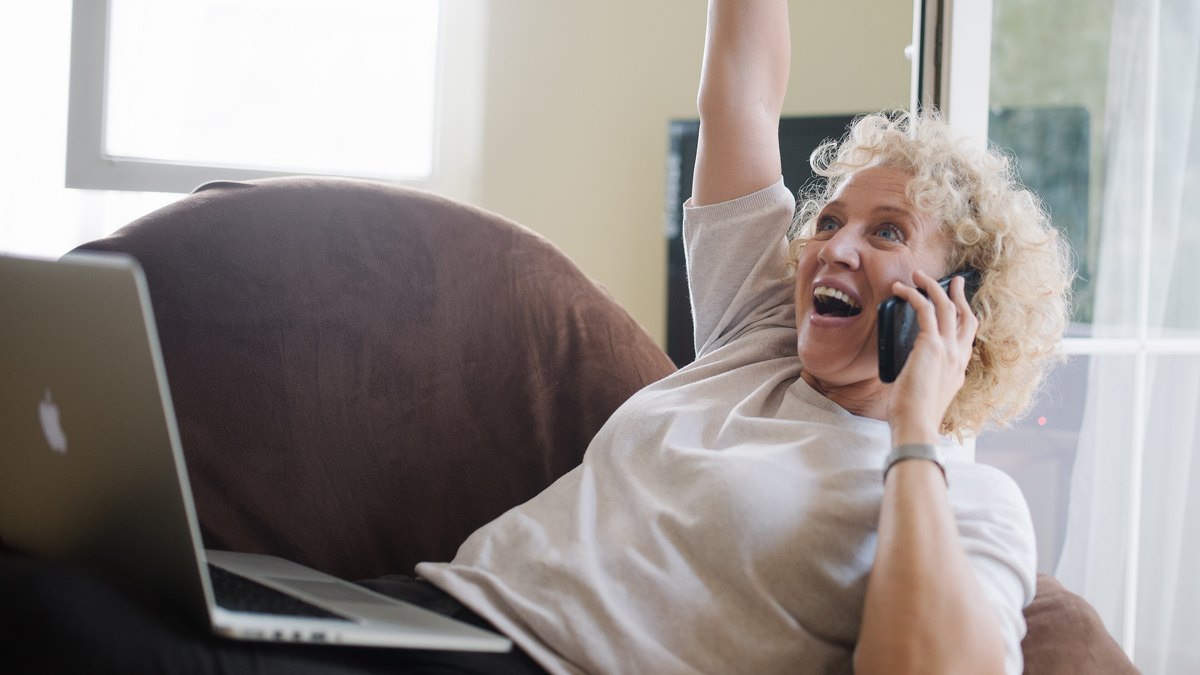 An older woman on a phone call with a laptop on her lap