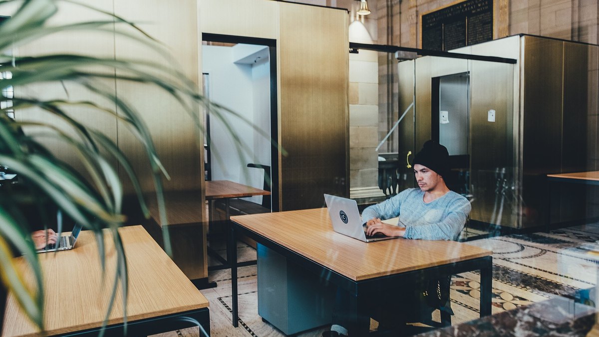 A person working at a laptop on a wooden desk in a bright shared office space