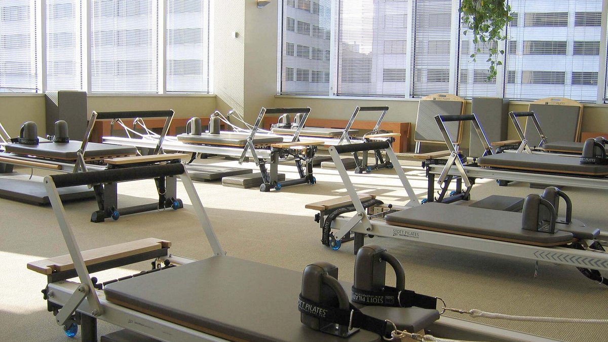 A bright Pilates studio with rows of STOTT PILATES reformers beside large windows