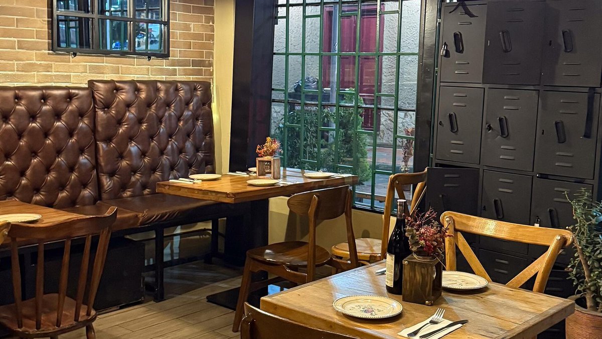 A restaurant dining room with a brick wall, a leather banquette and set tables