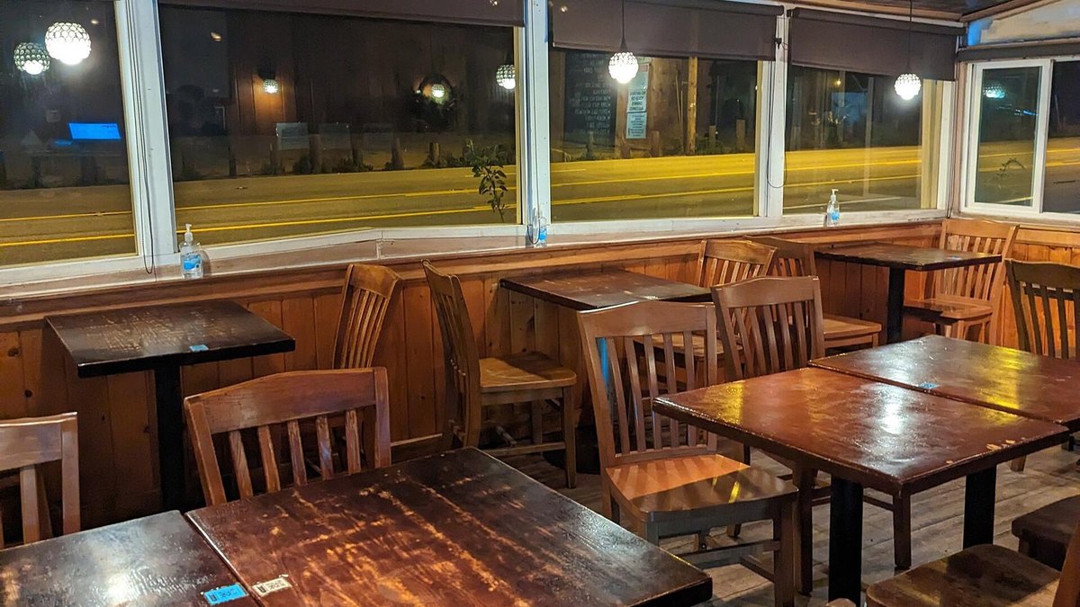 An empty restaurant dining room at night with wooden tables, chairs and window seating